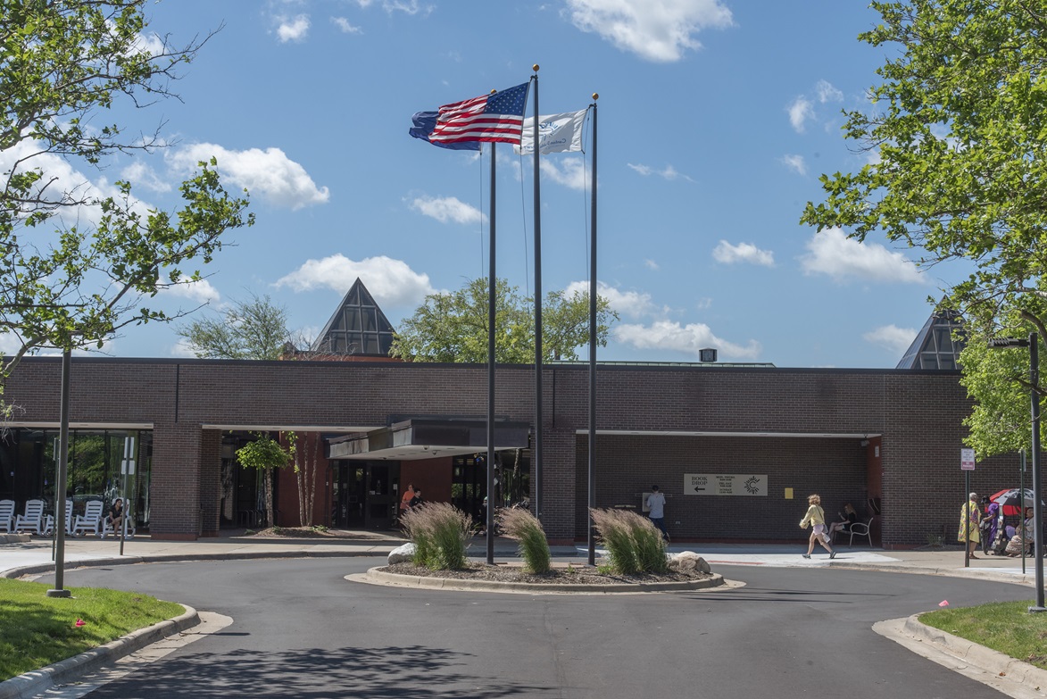 Canton Public Library entrance showing circle drive around a small mound of garden with flags of US and Michigan flying